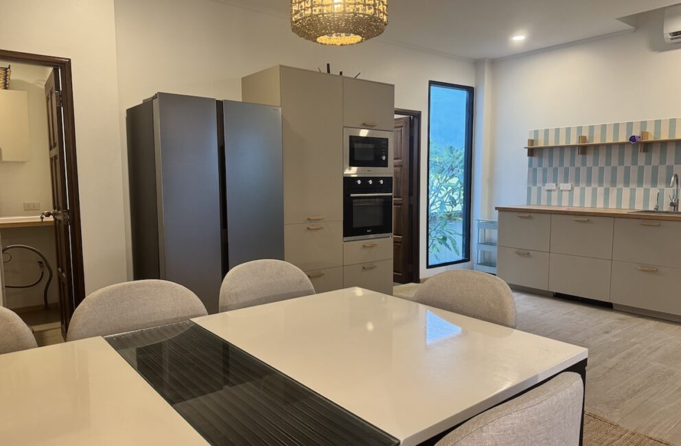 Open kitchen and dining area with a grey side-by-side fridge, built-in oven and microwave, and grey cabinets in Secret Garden Pool Villa B2
