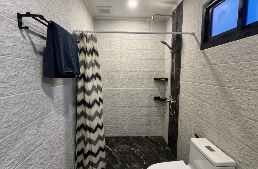 Shower with a zigzag-patterned curtain, textured white wall tiles, towel rail and a white toilet in Secret Garden Pool Villa B2